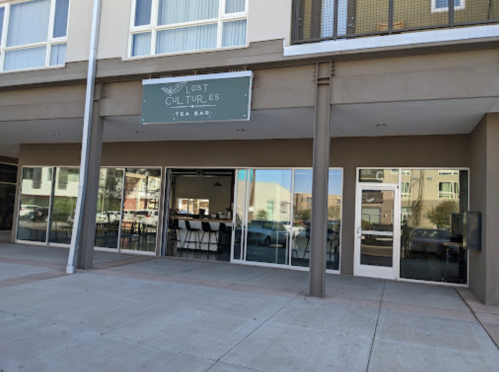 Exterior of "Lost Cultures Tea Bar," featuring large glass windows and a green sign above the entrance.